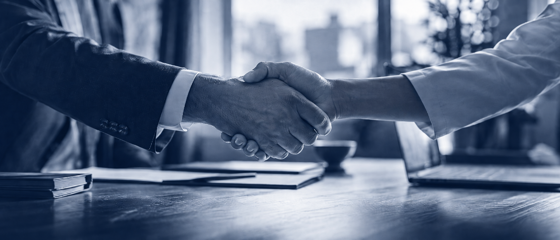 Two people shaking hands across a desk in a boardroom, rendered in navy duotone
