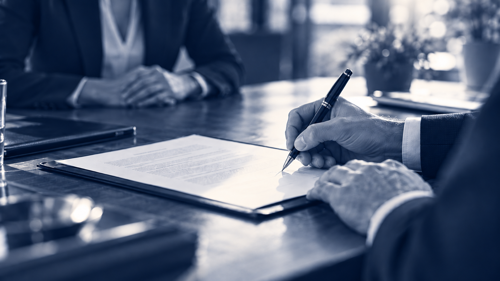 A hand signing transaction documents at a table